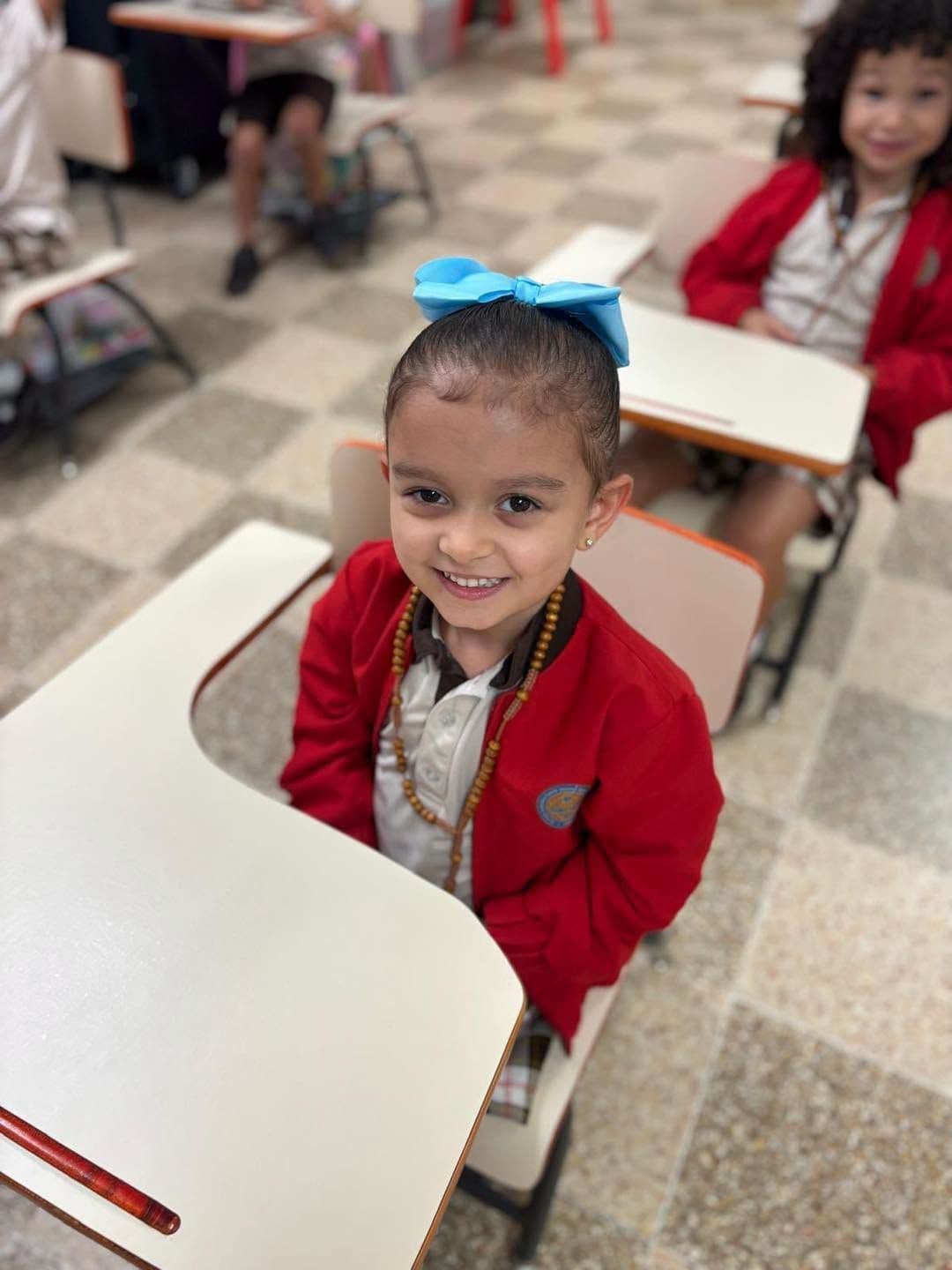 Niña de preescolar con lazo azul sentada en su pupitre