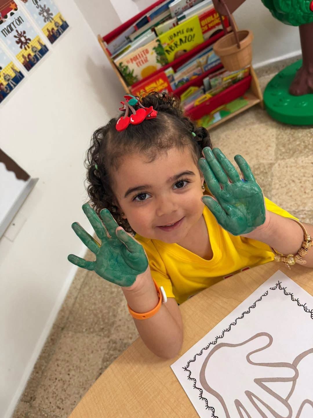 Niña de preescolar muestra sus manos pintadas de verde